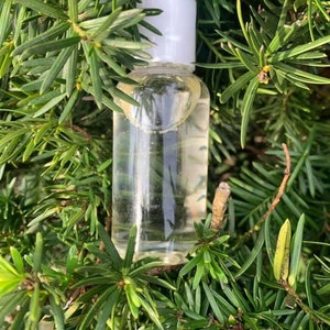 May include: A clear glass bottle with a white cap filled with a liquid. The bottle is sitting on a bed of green pine needles.