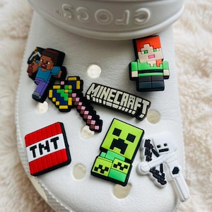 May include: White Crocs shoe with Minecraft themed shoe charms. The charms include a creeper, a skeleton, TNT, a pickaxe, a heart, a Steve character, and a Minecraft logo.