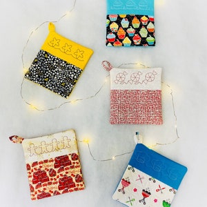 May include: Four colorful quilted pot holders with different designs. The pot holders have a loop handle and are made of cotton fabric. The designs include cupcakes, candy canes, gingerbread men, and a grill.