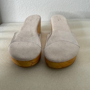 May include: A pair of white platform sandals with clear plastic straps. The sandals have a wooden platform and a suede upper.