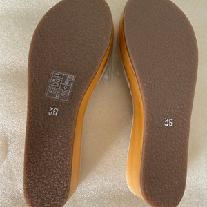May include: A pair of brown leather sandals with a wooden wedge heel. The sandals have a simple design and are made in India. The size is 36.