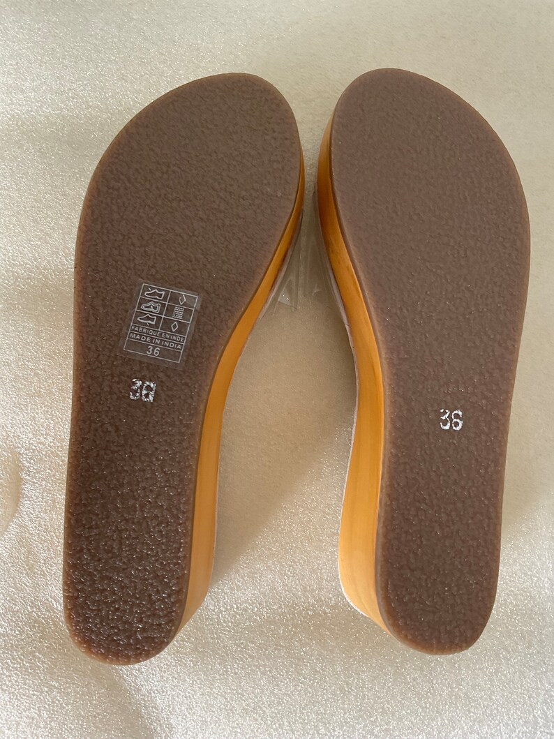 May include: A pair of brown leather sandals with a wooden wedge heel. The sandals have a simple design and are made in India. The size is 36.