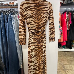 May include: A long, brown and white tiger print maxi dress with long sleeves and a tie belt. The dress is hanging on a rack in a clothing store.