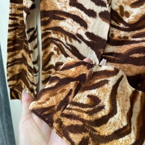 May include: Close-up of a brown and white tiger print long-sleeved shirt. The shirt has a soft, fuzzy texture.
