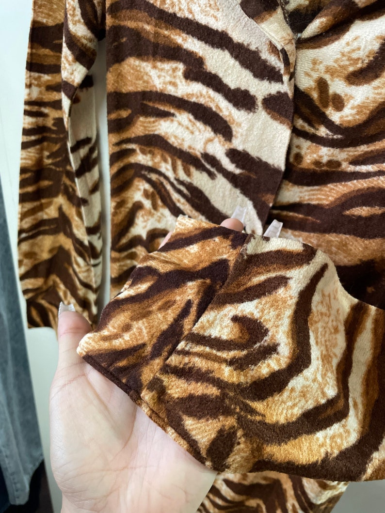 May include: Close-up of a brown and white tiger print long-sleeved shirt. The shirt has a soft, fuzzy texture.
