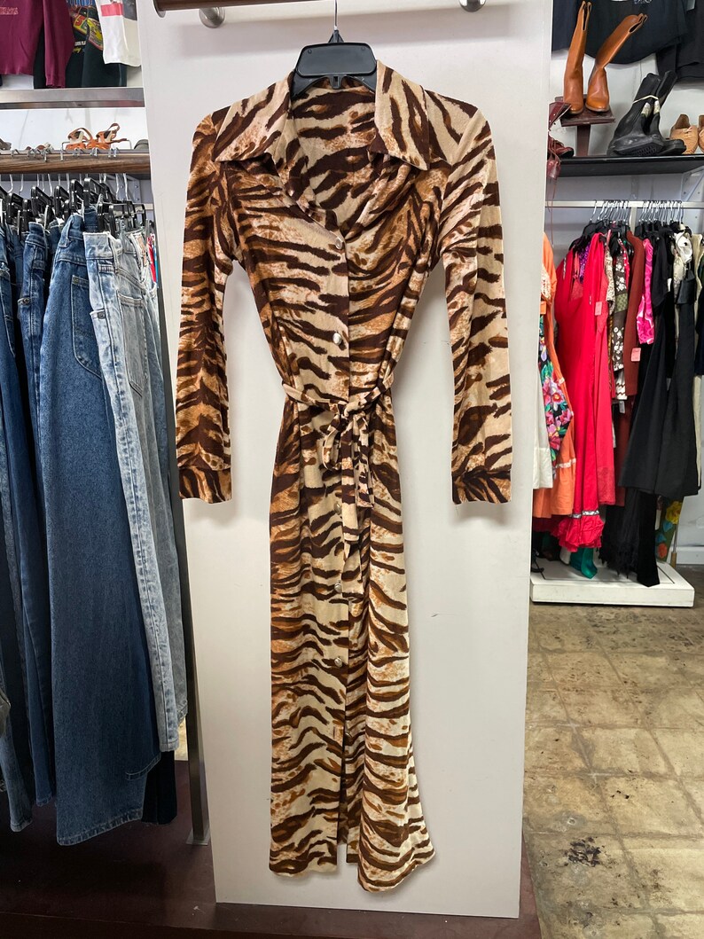 May include: A long-sleeved brown and white tiger print dress with a button-up front and a tie belt.