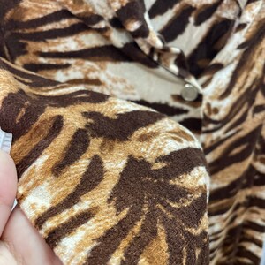 May include: Close-up of a brown and white animal print shirt with a button closure.