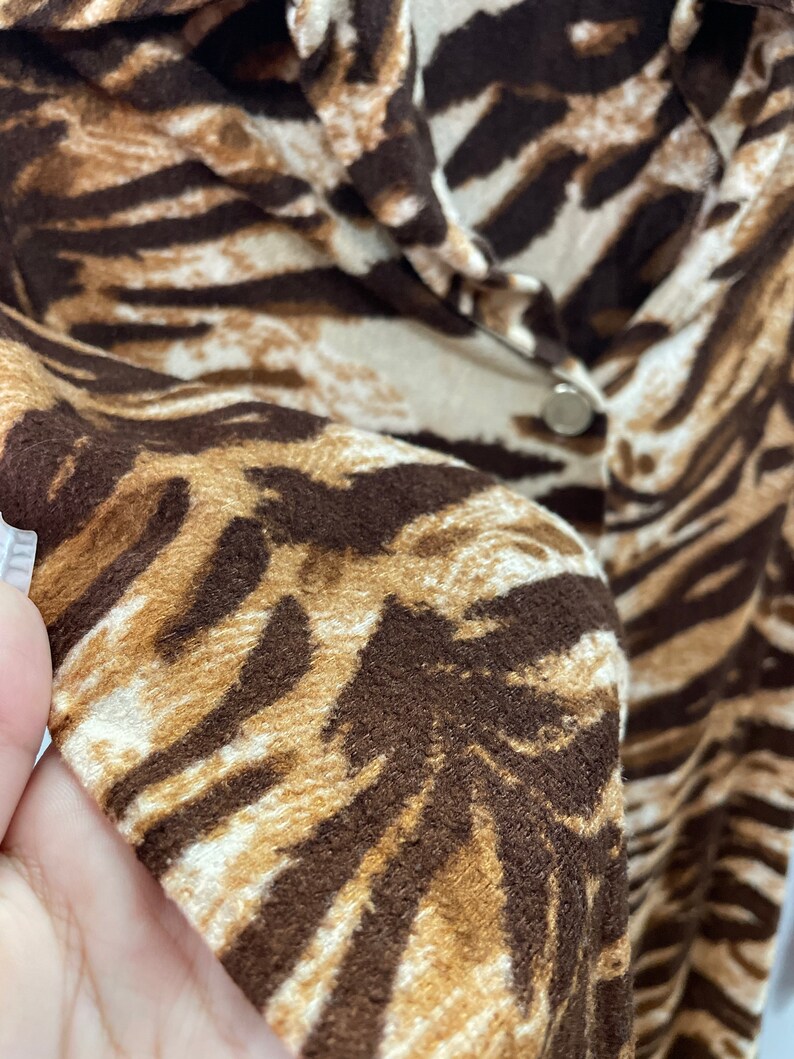 May include: Close-up of a brown and white animal print shirt with a button closure.