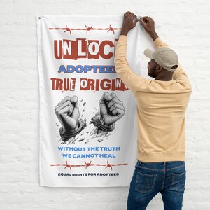 Op de afbeelding: Witte vlag met de woorden "UNLOCK ADOPTEES TRUE ORIGIN" in rood en blauw. Daaronder twee vuisten die zich bevrijden van handboeien. De vlag bevat ook de tekst "WITHOUT THE TRUTH WE CANNOT HEAL" en "EQUAL RIGHTS FOR ADOPTEES".