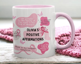 May include: White ceramic coffee mug with a pink rim and handle. The mug features a pink ribbon design with the text "Olivia's Positive Affirmations" and several inspirational quotes.