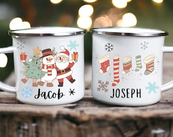 Könnte beinhalten: Zwei weiße Emaille-Tassen mit silbernen Rändern. Eine Tasse zeigt ein Design mit Weihnachtsbaum, Schneemann und Weihnachtsmann mit dem Namen "Jacob". Die andere Tasse zeigt Weihnachtsstrümpfe und den Namen "Joseph".