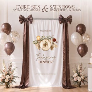 May include: A white fabric sign featuring the text "WELCOME TO Thanksgiving DINNER 14TH NOVEMBER 2026, NEW YORK" with a central illustration of a place setting, flanked by two long brown satin drapes topped with large brown satin bows.