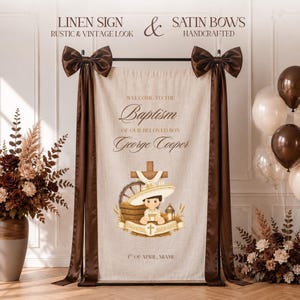 Puede incluir: Un letrero rectangular de lino beige con lazos de satén marrón en las esquinas superiores. El texto dice: Welcome to the Baptism of our beloved son George Cooper, 1st of April, Miami. Incluye un gráfico de un niño, una cruz y una rueda.