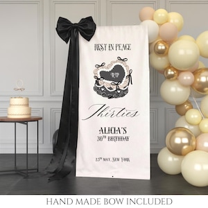 Może przedstawiać: Biały baner z czarnym tekstem i czarną kokardą. Na banerze widnieje napis "Rest in Peace" i "Thirties" z "Alicia's 30th Birthday" i datą. Widoczny jest również dwupiętrowy tort i łuk balonowy.