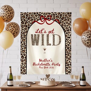May include: A party scene with balloons, champagne, and a cake. The focal point is a sign that reads "Let's get WILD" with "Heather's Bachelorette Party New York 2026" below. Leopard print balloons and accents are featured.