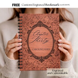 May include: A wooden spiral-bound notebook with the text "Chapter Thirty" and the name "CAROLINE JAMES" in an ornate oval frame. The cover has a floral pattern and is labeled "Engraved and Customizable".