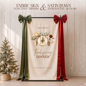 May include: A cream-colored fabric sign hanging on a black metal stand, featuring a printed illustration of a place setting, the text "WELCOME TO Thanksgiving DINNER 14TH NOVEMBER 2016, NEW YORK," and large olive green and deep red satin bows.