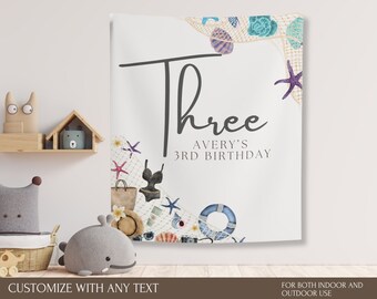May include: White banner with the word "Three" and "Avery's 3rd Birthday" in black script. The banner is decorated with watercolor illustrations of seashells, starfish, a swimsuit, and a beach bag. Text at the bottom says "Customize with any text" and "For both indoor and outdoor use."