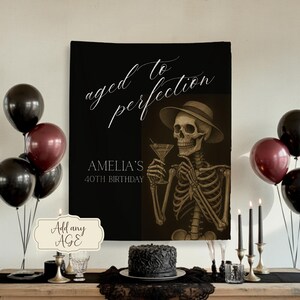 Può includere: Un banner nero con la scritta "aged to perfection" e "Amelia's 40th Birthday" è esposto. Uno scheletro con un cappello che tiene in mano un bicchiere da martini è sul banner. Palloncini neri e bordeaux, una torta e candele sono su un tavolo.