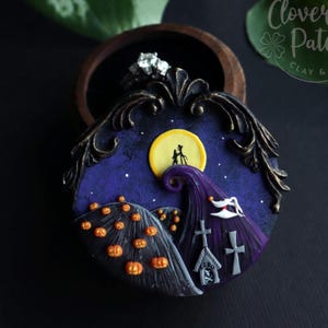 May include: A handcrafted ring box with a whimsical design inspired by "The Nightmare Before Christmas." The box features a night sky with a full moon, a purple hill, and a graveyard scene with pumpkins. The ring is visible inside the box.