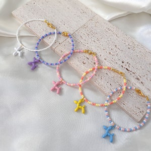 May include: Four colorful beaded bracelets with balloon dog charms. The bracelets are in shades of white, purple, pink, yellow, and blue.