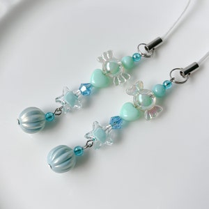 May include: A light blue and clear phone charm with a candy, heart, star, and bead design.