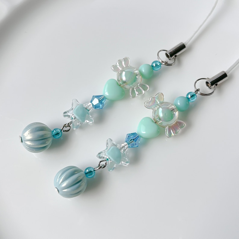 May include: A light blue and clear phone charm with a candy, heart, star, and bead design.