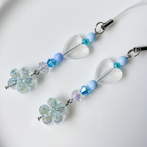 May include: A light blue and clear phone charm with two clear heart-shaped beads, two iridescent flower-shaped beads, and blue and clear crystal beads.