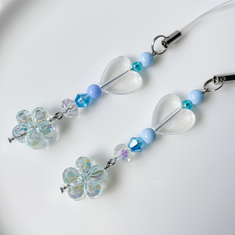 May include: A light blue and clear phone charm with two clear heart-shaped beads, two iridescent flower-shaped beads, and blue and clear crystal beads.