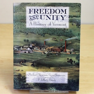 Op de afbeelding: Een hardcover boek met de titel "FREEDOM and UNITY: A History of Vermont." De omslag toont een vintage illustratie van een landelijk landschap met gebouwen, bomen en schoorstenen. De namen van de auteurs staan onder de titel.
