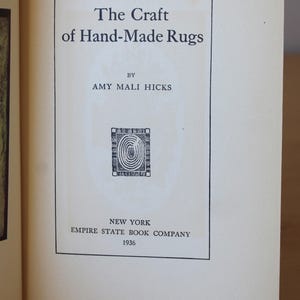 May include: The cover of a book titled "The Craft of Hand-Made Rugs" by Amy Mali Hicks. The book was published in 1936 by the Empire State Book Company in New York.