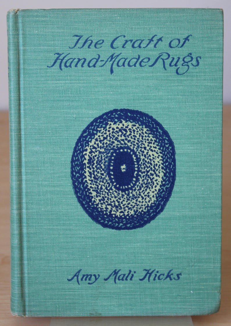 May include: A teal blue book with the title "The Craft of Hand-Made Rugs" in dark blue lettering. The cover features a blue and white circular design with a smaller blue circle in the center.