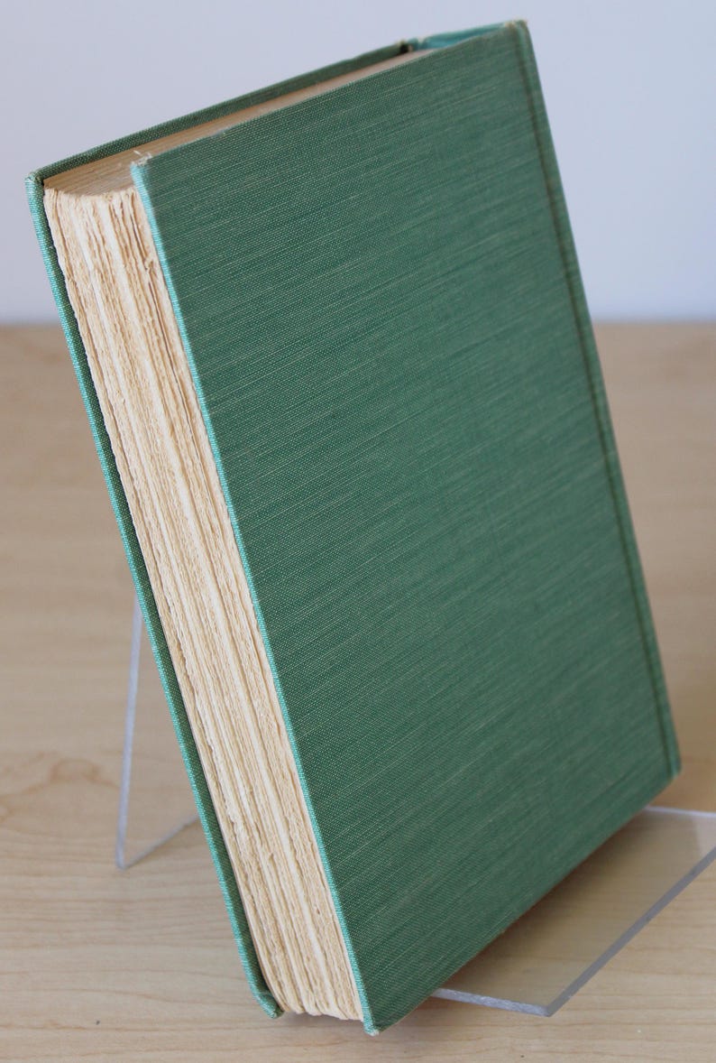 May include: A green hardcover book with a spine that is slightly worn. The book is standing upright on a clear acrylic bookend.