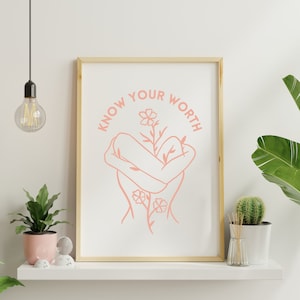 May include: A framed print with a pink line drawing of a person holding a flower. The text "KNOW YOUR WORTH" is written in a circle around the person.