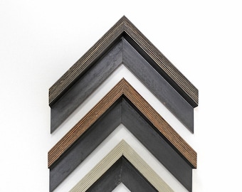 May include: An assortment of wooden picture frame corners in various colors, including dark brown, light brown, black, beige, and white. The frames are arranged in a chevron pattern against a white background, showcasing different design options.