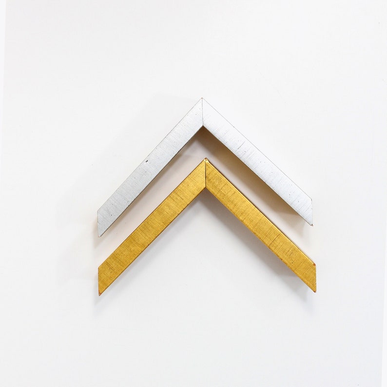May include: Two picture frames, one silver and one gold, are shown in a close-up view. The frames are angled to form a point at the top.