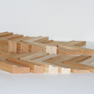 May include: A collection of various sizes and styles of unfinished wood picture frames. The frames are arranged in a staggered pattern, showcasing the different widths and profiles.