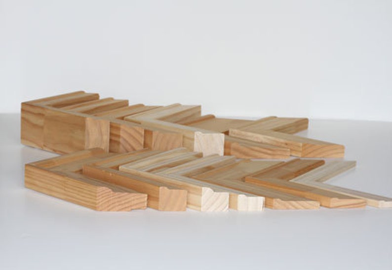 May include: A collection of various sizes and styles of unfinished wood picture frames. The frames are arranged in a staggered pattern, showcasing the different widths and profiles.