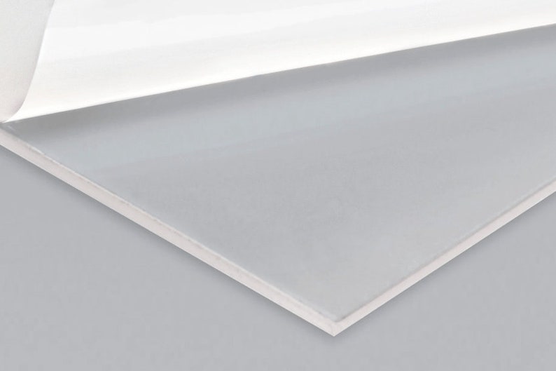May include: A white sheet of adhesive-backed paper with a clear plastic sheet attached to it. The plastic sheet is partially peeled back to reveal the adhesive.