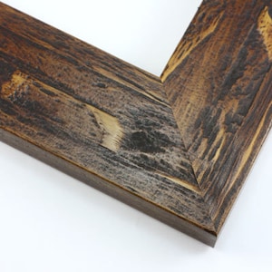 May include: Close-up of a corner of a rustic wooden picture frame. The frame has a distressed finish with shades of brown, gray, and tan, showcasing the natural wood grain. The corner is joined at a 45-degree angle.