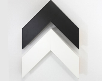 May include: Two picture frames, one black and one white, are stacked on top of each other in the shape of an arrow pointing upwards.