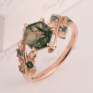 May include: A rose gold ring with a green moss agate gemstone and a leafy design. The leaves are accented with smaller green gemstones.