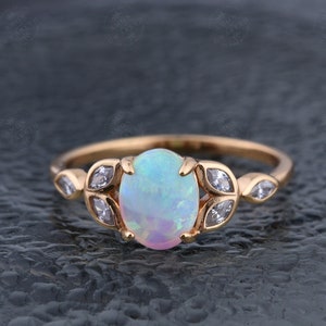 May include: A delicate gold ring with a large oval opal gemstone surrounded by smaller clear gemstones set in a leaf design.