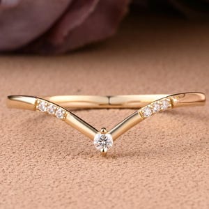 May include: A delicate gold ring with a V-shaped band and small diamonds set along the edges. The ring has a single, larger diamond at the point of the V.