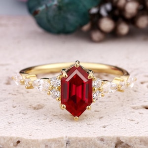 May include: A gold ring with a large, octagon-shaped ruby gemstone surrounded by smaller, white diamonds. The ring has a delicate, vintage-inspired design.