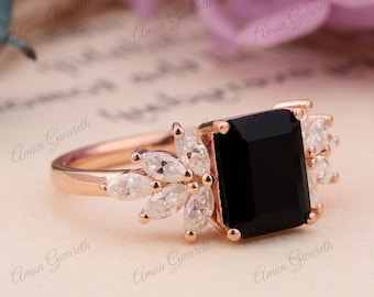 Könnte beinhalten: Ein Ring aus Roségold mit einem großen schwarzen quadratischen Edelstein und einem Cluster kleinerer klarer Edelsteine auf der Ringschiene.