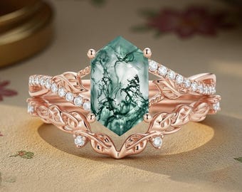 Peut inclure: Un ensemble de bagues en or rose avec une pierre de moss agate verte hexagonale. La bague de fiançailles présente un motif de feuilles avec de petites pierres claires. L'alliance assortie a un motif de feuilles similaire avec de petites pierres claires.