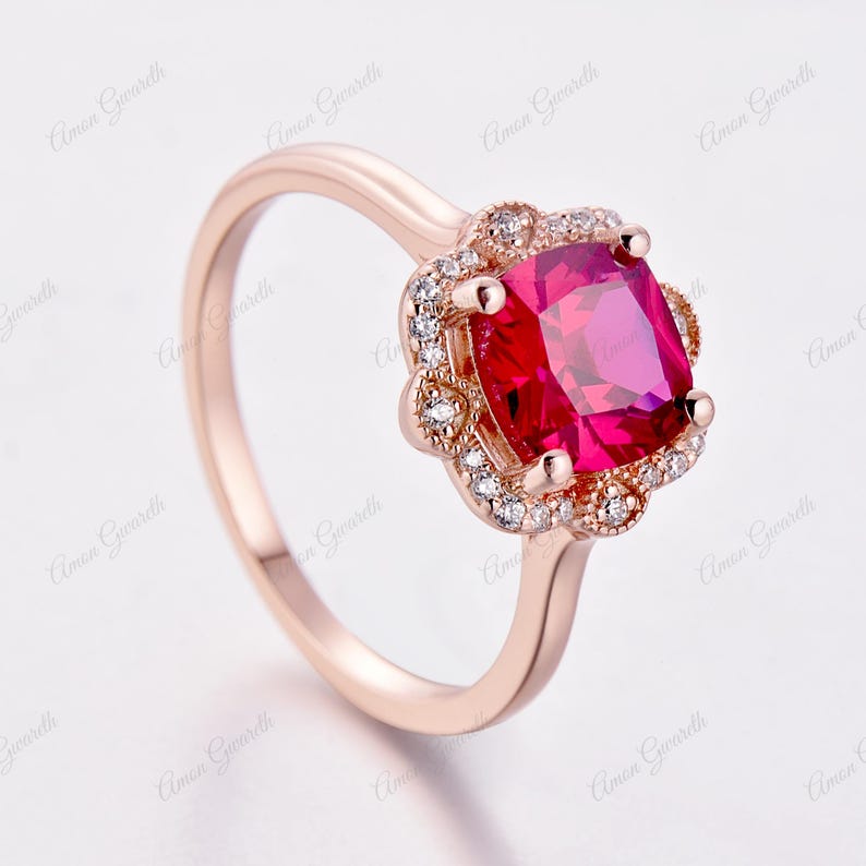 May include: A rose gold ring featuring a large, square-shaped, red gemstone surrounded by a halo of smaller, clear gemstones.