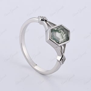 Puede incluir: Un anillo de plata con una piedra preciosa verde hexagonal y dos peque&ntilde;as piedras preciosas transparentes en la banda.