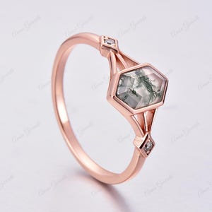 Puede incluir: Un anillo de oro rosa con una piedra hexagonal de &aacute;gata verde musgo y dos peque&ntilde;os diamantes. El anillo tiene un dise&ntilde;o geom&eacute;trico.